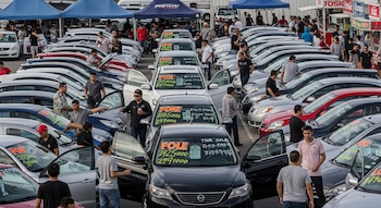 Vista aérea de un concurrido mercado al aire libre con cientos de autos usados estacionados en filas y muchas personas examinándolos.
