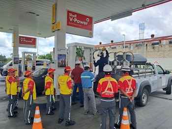 Técnicos con cascos de seguridad y personal con chalecos amarillos rodean un surtidor de combustible y una camioneta blanca