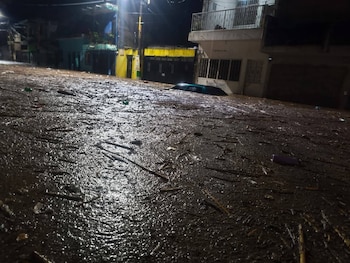 Vista nocturna de una calle inundada y cubierta de escombros en una zona urbana de Ciudad de Guatemala, con un coche parcialmente sumergido y edificios a lo lejos