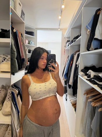 Oriana Sabatini, embarazada, se toma una selfie en un espejo mostrando su barriga en un top blanco y pantalones grises, en un vestidor