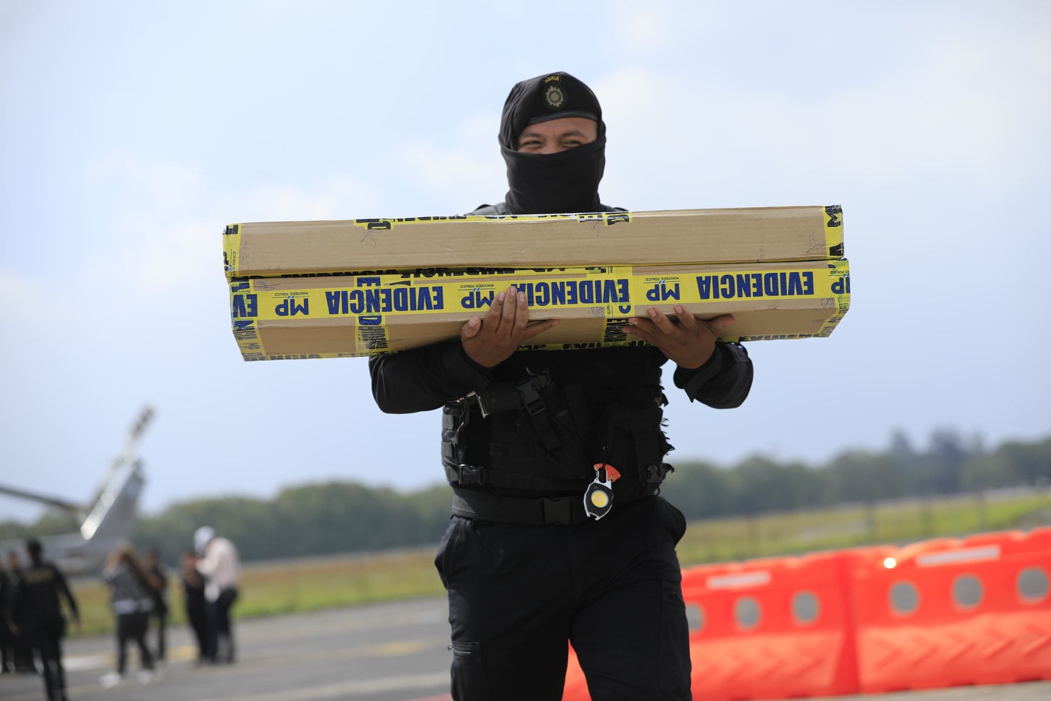 Un agente de seguridad con equipo táctico transporta dos paquetes de evidencia marcados con 'MP' y 'EVIDENCIA', posiblemente tras un operativo. (Ministerio de Gobernación de Guatemala)