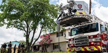 Un camión de bomberos con plataforma elevada y varios bomberos uniformados ante una vivienda de dos plantas y un árbol