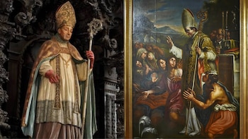 Estatua de un obispo con mitra y báculo en un altar, junto a una pintura que muestra a un obispo bendiciendo a un grupo de personas con un hombre arrodillado