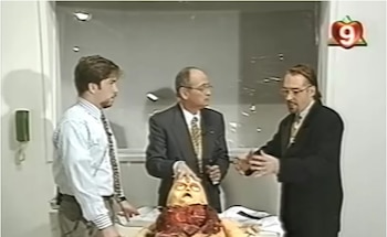 Tres hombres con traje rodean una mesa sobre la que yace la figura de una criatura extraterrestre dentro de un estudio