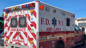 Vista lateral y trasera de una ambulancia blanca y roja del FDNY con luces de emergencia y la insignia de la Estrella de la Vida