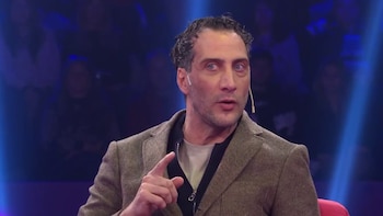 Luciano Cáceres, hombre de cabello rizado oscuro, ojos azules y barba incipiente, viste una chaqueta tweed marrón y camiseta beige, señalando con su mano derecha mientras habla