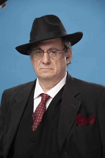 Retrato de un hombre de mediana edad, con sombrero negro, gafas redondas, traje oscuro, chaleco, camisa blanca y corbata roja estampada, sobre fondo azul