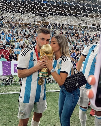 Nicolás Tagliafico y Carolina Calvagni besan la Copa del Mundo en un campo de fútbol con la red de la portería y la multitud de fondo