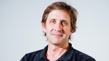 Un hombre caucásico de mediana edad con cabello castaño y camisa polo negra está de pie con los brazos cruzados, sonriendo ligeramente