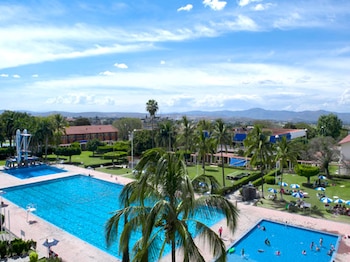 Vista aérea de varias piscinas, trampolines, palmeras, césped, edificios, sombrillas y personas en un complejo