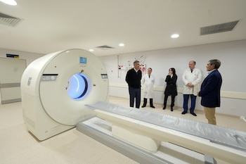 Un tomógrafo grande de color blanco en una sala médica iluminada junto a cinco personas, dos con bata blanca
