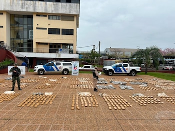 Dos hombres uniformados y armados junto a dos camionetas de Prefectura Naval Argentina. En el suelo hay cientos de bloques rectangulares y bolsas con sustancias