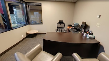 Interior de oficina con escritorio, silla de oficina, monitor, teclado, ratón, dos sillones, mesa auxiliar, ventana grande y paredes