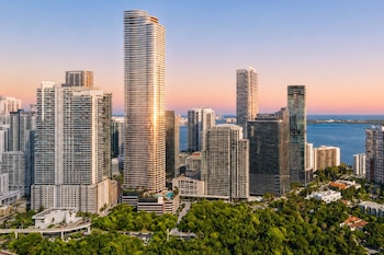 Vista aérea de un paisaje urbano con rascacielos, edificios, abundante vegetación, una bahía y cielo al atardecer en Miami