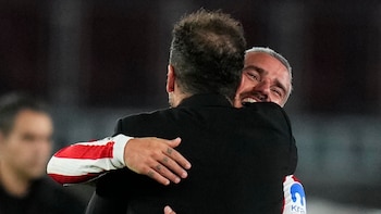 Vista trasera de Diego Simeone abrazando a Antoine Griezmann, quien sonríe mostrando su rostro con cabello gris y barba, vestido con una camiseta rojiblanca