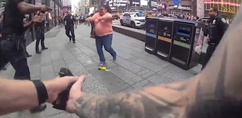 Fotograma de cámara corporal donde oficiales de policía apuntan sus armas a una mujer con camiseta rosa en una calle de la ciudad