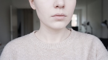 Primer plano de una persona mostrando la parte inferior de la cara y el cuello, con piel clara y labios claros, vistiendo un suéter beige.