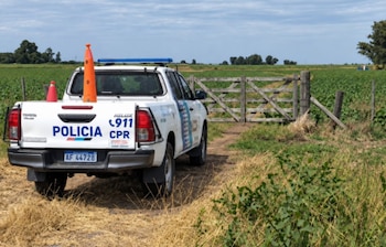 Camioneta policial blanca estacionada en un camino de tierra frente a una tranquera de madera y un campo de cultivo
