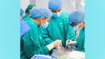 Tres profesionales de la salud con uniformes quirúrgicos verdes, gorros azules y mascarillas blancas realizan una intervención con instrumental