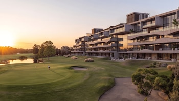 Edificio residencial con terrazas junto a un campo de golf con dos personas en el césped, trampas de arena y un lago al atardecer