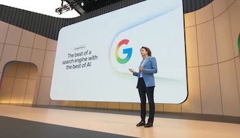 Una mujer en un escenario presenta Google Search en una pantalla grande, mostrando el logo de Google y texto sobre la integración de IA