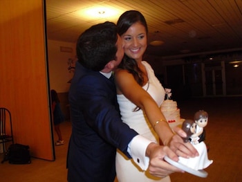 Maje Moreno Cantó con hombre de traje oscuro, se abrazan y sostienen figura de novios. Pastel de bodas y niña en el fondo de una celebración