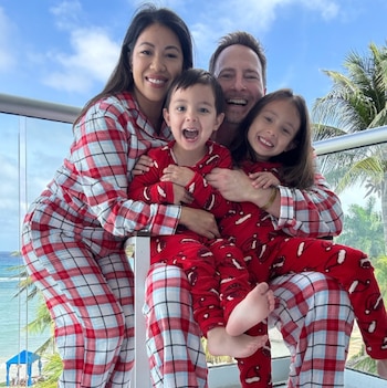 Una familia feliz de cuatro personas, madre, padre y dos hijos, vistiendo pijamas a cuadros y rojas, posando en un balcón con el océano de fondo
