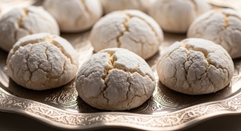 Primer plano de varias galletas argelinas de almendra cubiertas de azúcar glas, sobre una bandeja metálica tradicional del Magreb con grabados.