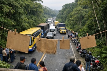 Vista aérea de una larga fila de autobuses, camiones y motos detenidas en una carretera selvática, con personas esperando y carteles improvisados colgando en primer plano.