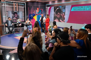 Vista general de un estudio de televisión con tres presentadores, pantallas grandes mostrando a Maluma y una audiencia grabando con sus teléfonos
