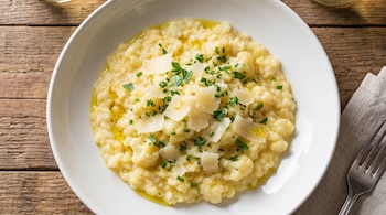 Risotto cremoso de coliflor en un cuenco blanco sobre mesa de madera, con parmesano, perejil y aceite de oliva. Vista cenital.