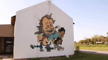 Mural colorido en la pared blanca de un edificio, con una caricatura de un hombre barbudo y sonriente rodeado de cuatro niños, bajo un cielo claro