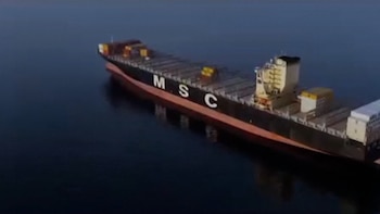 Vista aérea de un gran buque portacontenedores de color oscuro con la inscripción blanca "MSC" en el costado, navegando en aguas tranquilas y azules. Se aprecian contenedores en la cubierta