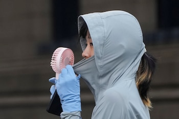 Una mujer usa un ventilador mientras usa un paño que la protege del sol en una calle (REUTERS/Aly Song)