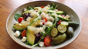 Un tazón de cerámica con ensalada de aguacate, tomates, queso, hojas verdes, perlas de lima dedo y frutos de lima dedo enteros.