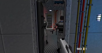 Captura de pantalla de Goldeneye 007. Dos figuras armadas en un pasillo gris metálico con puertas, cables de colores en la pared y un arma en primer plano