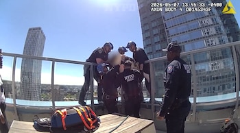 Varios agentes del NYPD rescatan a una persona en el borde de la azotea de un rascacielos. Equipo de rescate visible, ciudad y cielo azul de fondo