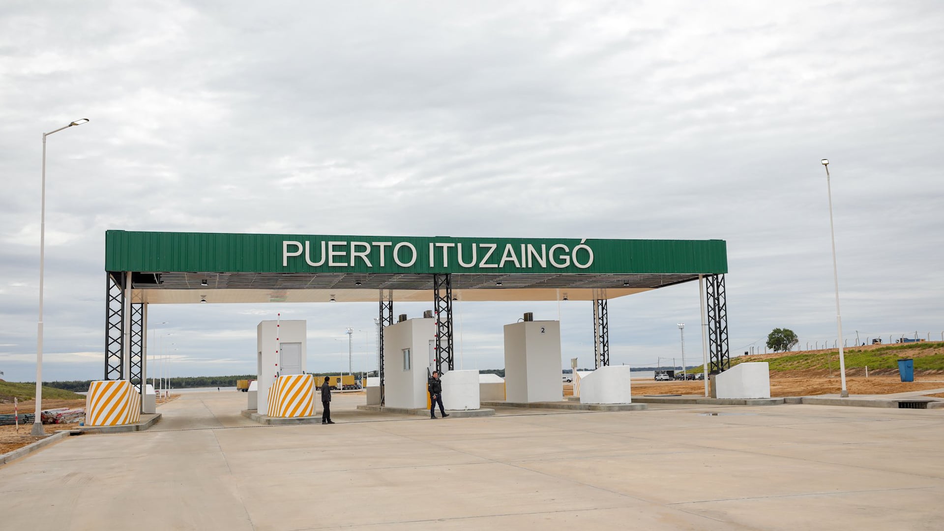 La entrada principal del Puerto Ituzaingó muestra una estructura verde con el nombre del puerto, varias garitas y dos hombres de pie en la zona de control.