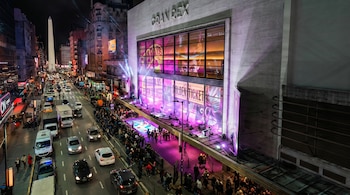 Vista aérea nocturna de la Avenida Corrientes en Buenos Aires. El Teatro Gran Rex iluminado en rosa y púrpura, multitud en la acera y tráfico de vehículos.