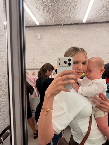 Eva Bargiela, mujer rubia, se toma una selfie en un espejo sosteniendo a su bebé Faustino dormido. Lleva una camiseta blanca y una pulsera dorada