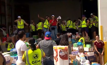 Un grupo de personas, muchas con chalecos amarillos, manipula cajas y paquetes de ayuda en una zona de carga