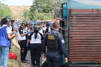 Bomberos Voluntarios y agentes de la PNC se encuentran junto a un autobús volcado en el borde de una carretera, con árboles y colinas al fondo