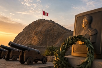 Cañones antiguos, una placa de bronce con una corona de laureles y el Morro Solar con la bandera de Perú en la cima al amanecer.