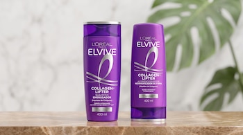 Dos envases morados de productos para el cabello sobre una mesa de mármol ante un fondo desenfocado con una hoja verde.