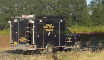 Camión azul de la Policía Estatal de Oregón con la leyenda Oregon State Police Forensics en un camino rural rodeado de vegetación