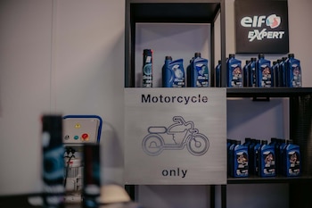 Estantería negra con botellas azules de lubricantes Elf Expert para motocicleta. Un cartel plateado con el texto 'Motorcycle only' y un icono de moto. Un letrero 'Elf Expert'