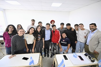 Un grupo de jóvenes y adultos posa sonriendo en un aula con pupitres blancos y pequeñas banderas argentinas