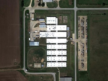Imagen satelital de un complejo penitenciario con edificios blancos, canchas, estacionamientos con vehículos, zonas verdes y campos agrícolas