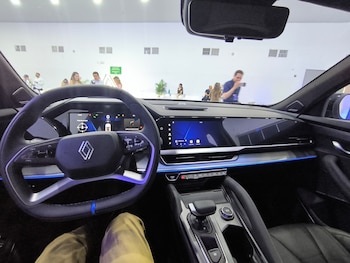 Vista interior de un automóvil con volante de la marca Renault, tres pantallas en el tablero y personas visibles a través del parabrisas