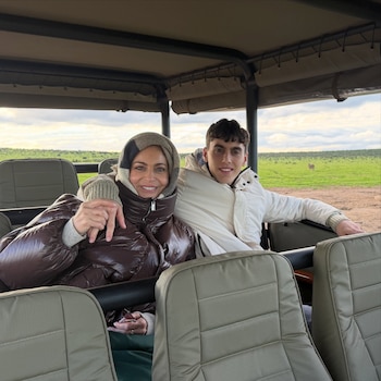 Una mujer y un hombre dentro de un vehículo de safari con techo de lona, asientos color caqui y paisaje verde con un animal a la distancia